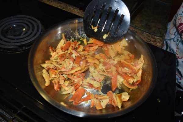 An image of Chicken of the Woods mushrooms being cooked in a pan; they are orange and yellow and appear similar to orange peels.