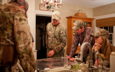 An image of several people in camouflage inside a house getting ready to go hunt
