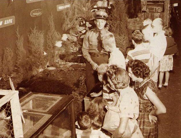 An black and white image of a game warden talking to children