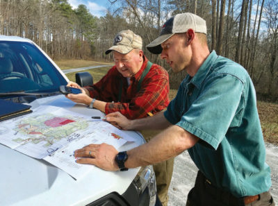 An image of two men looking at a map which has been placed on the hood of a white truck as they decide where they will place their nesting boxes.