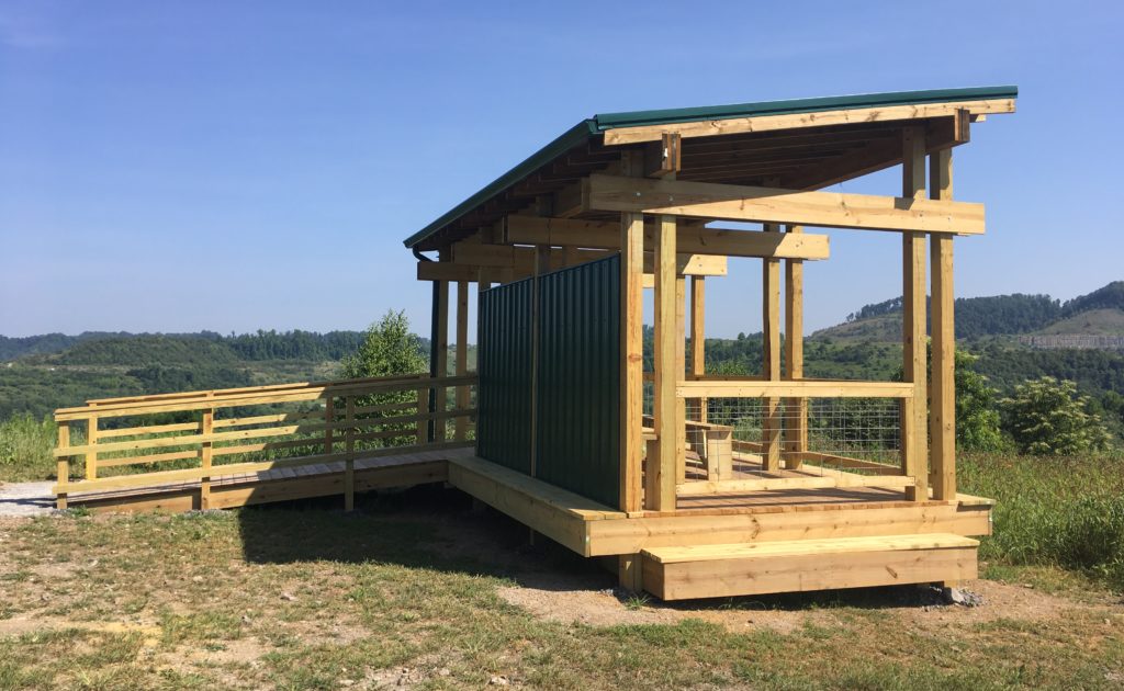 An image of an elk viewing station which appears to be a wooden pavilion with a tin roof and walls; overlooks a meadow and natural outlook as it is on a hill.