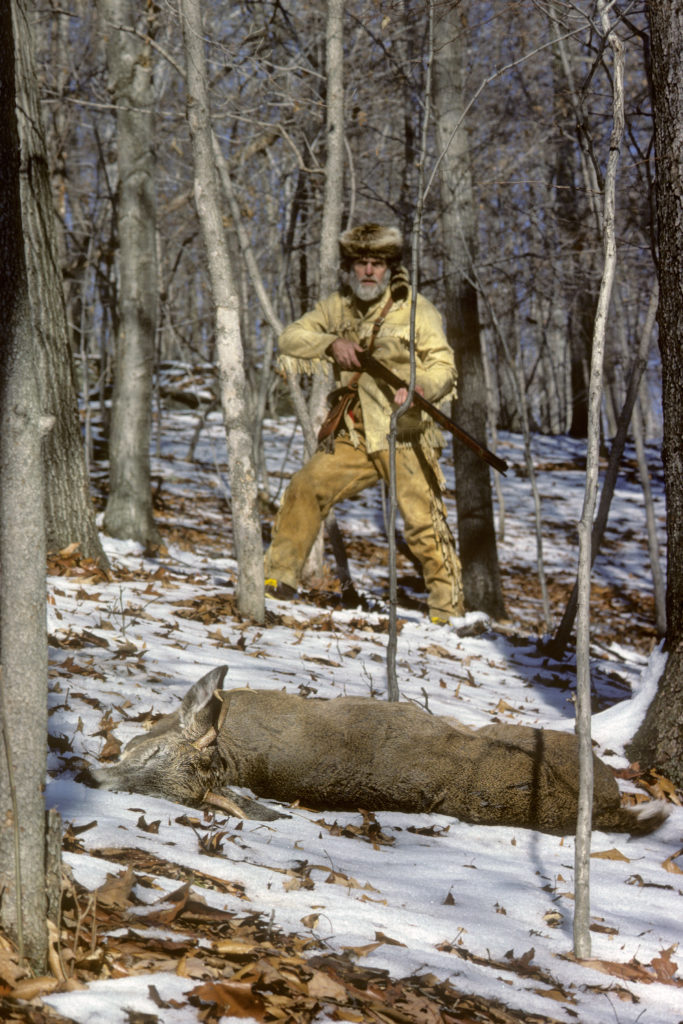 An image of a hunter with a dead deer in front of him that he had shot with a muzzleloader rifle
