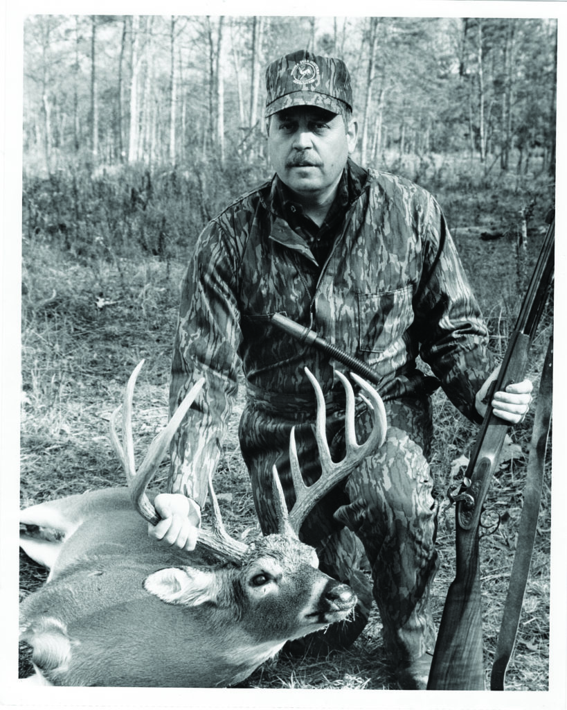 A black and white photo of a man, a deer and a muzzle loading rifle
