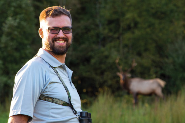 An image of a man with an elk in the background