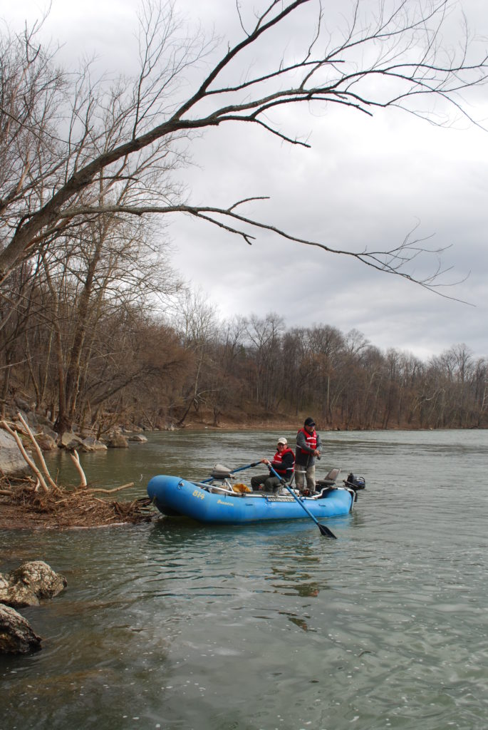 An image of two people fishing in red lifejackets upon a blue raft in New River; it's important to travel with a buddy in the outdoors especially in hazardous weather or temperatures.
