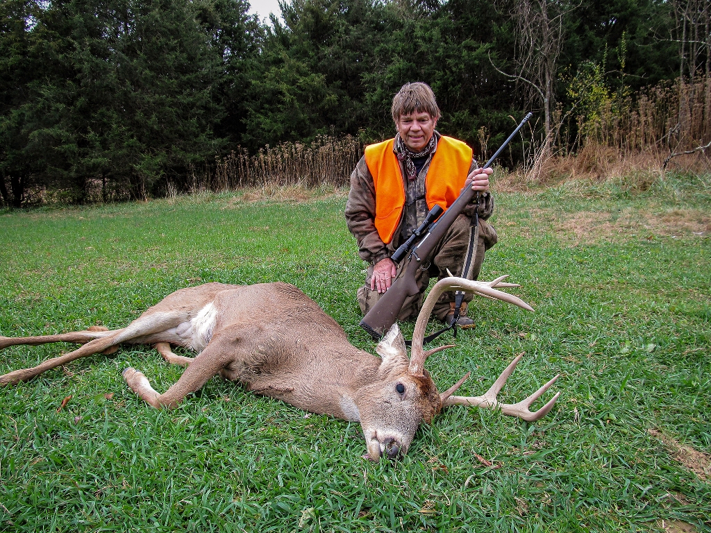 An image of a man with an orange visibility vest posing in front of a bull deer he has shot