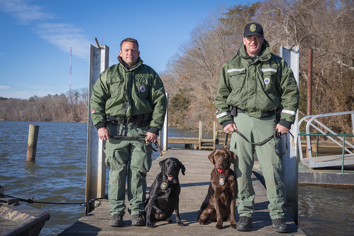 CPO James Patrillo and K9 Bailey (left) and Senior CPO Wes Billings and K9 Molly on a dock.