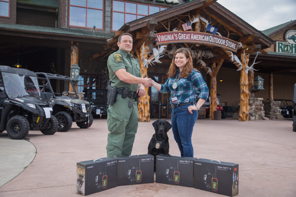 An image in front of Bass Pro Shops of K9 CPO bailey the black lab accepting donated GPS tracking collars for the new K9 trainees