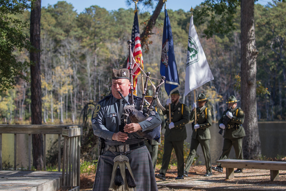 An image of a man with bagpipes leading a DWR honor guard dedication ceremony in a deciduous forest