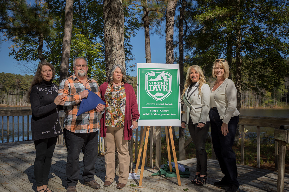 An image of the five members of the Gentry family taking a photo with the Virginia state flag in front of a sign of the DWR logo