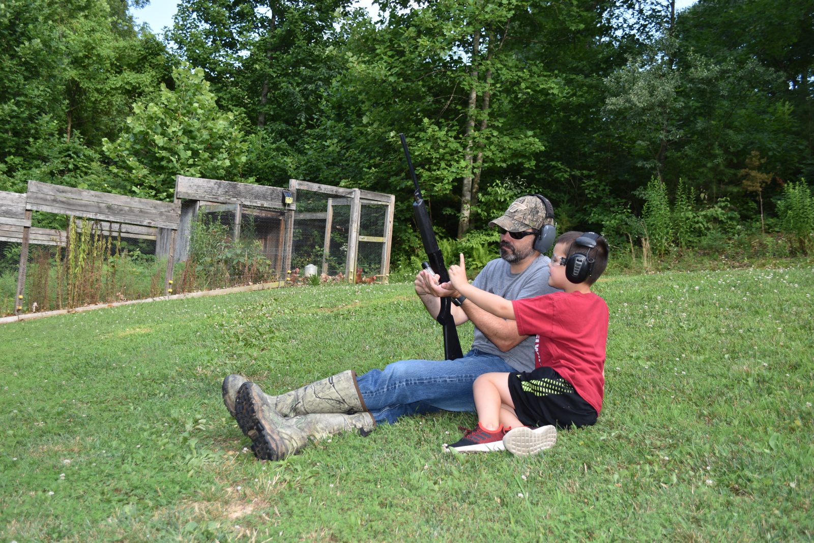 An image of a young child and their father sitting in a meadow with a gun reviewing gun safety