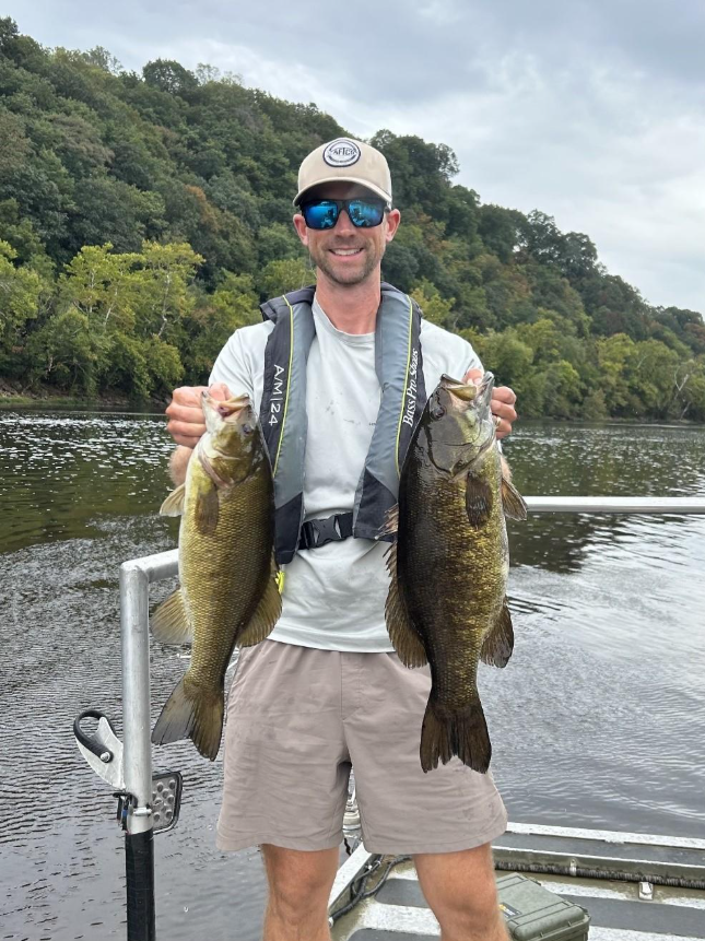 Angler standing on a boat and holding two smallmouth bass on the Upper James River.