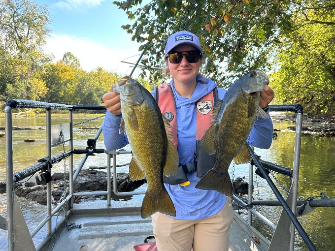 Angler on a boat holding two bass on the South Fork Shenandoah River.