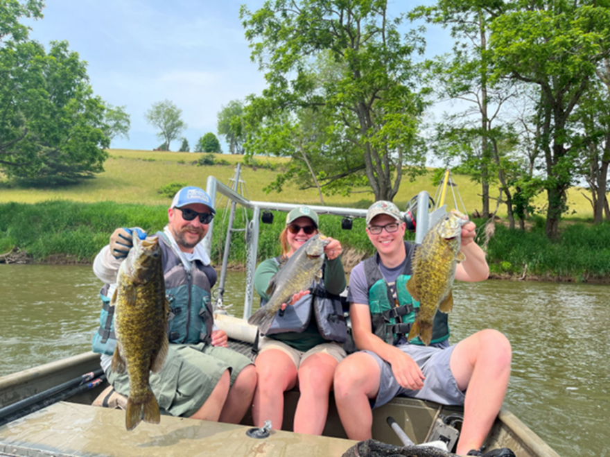 Three anglers seated on a boat holding fish on the Upper New River.