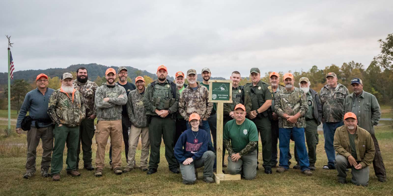 A group of 20 people posing as a group with a sign that reads "Elk Weigh Station."