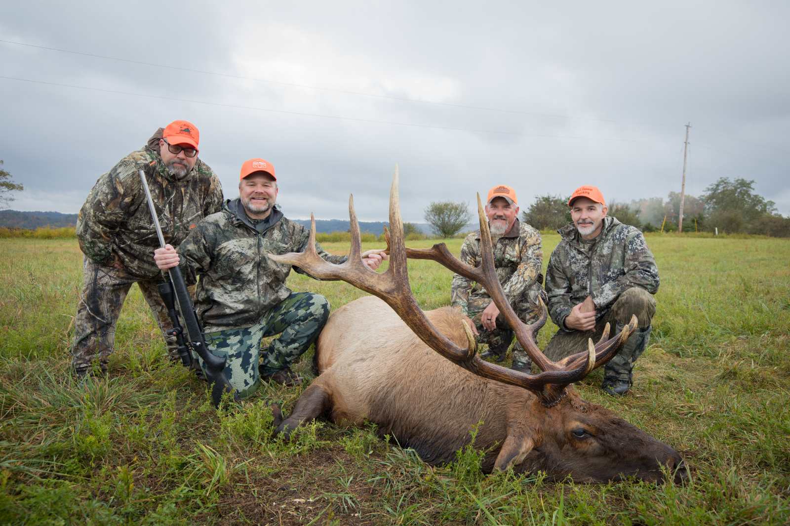 Four hunters in camoflague and blaze orange posing with a harvested bull elk.