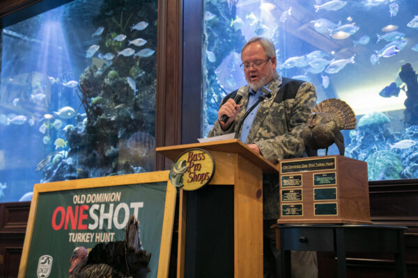 An image of an man giving out a trophy in front of a giant fish tank at Bass Pro Shops