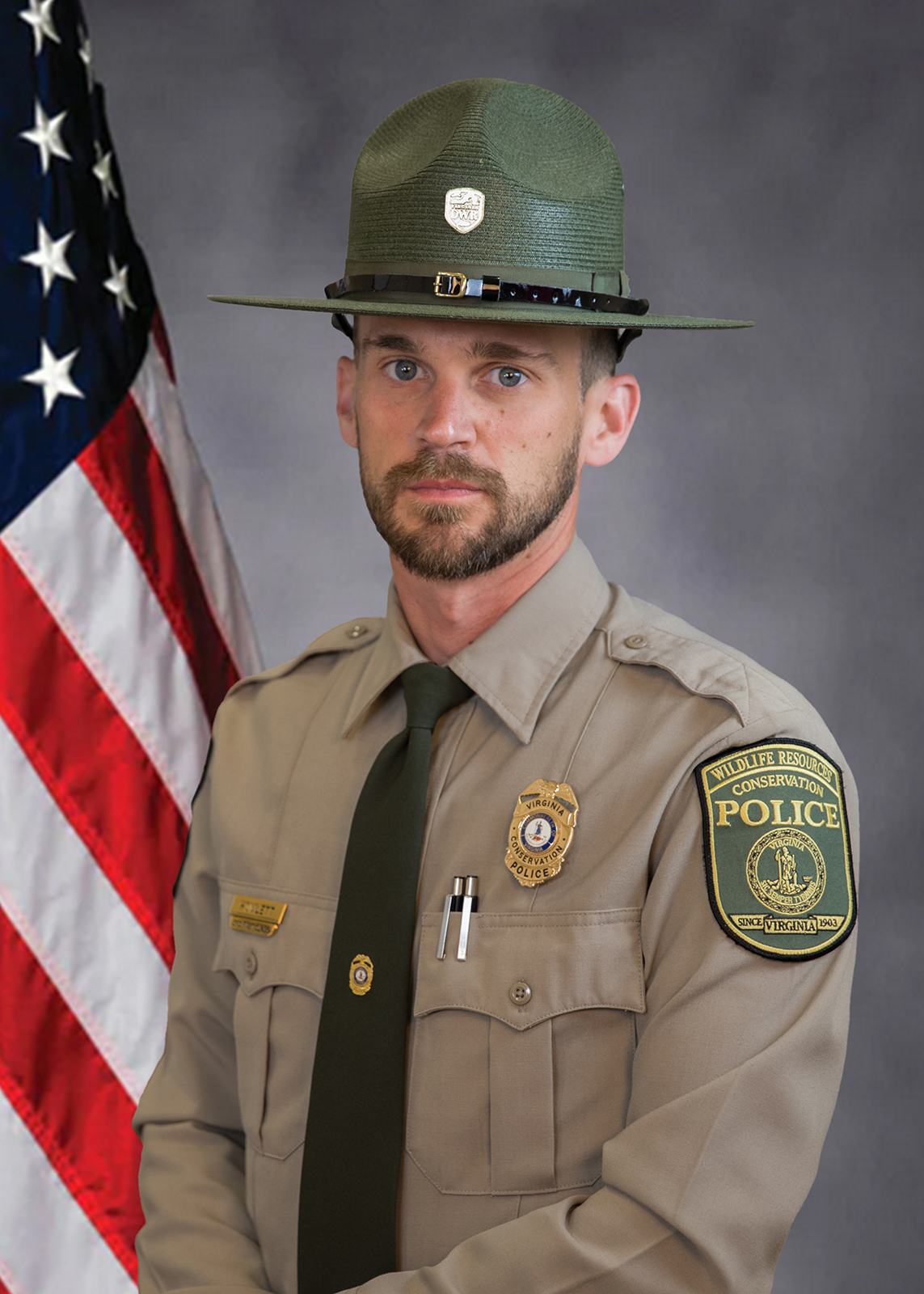 A photo of a Conservation Police Officer with an American flag posing.