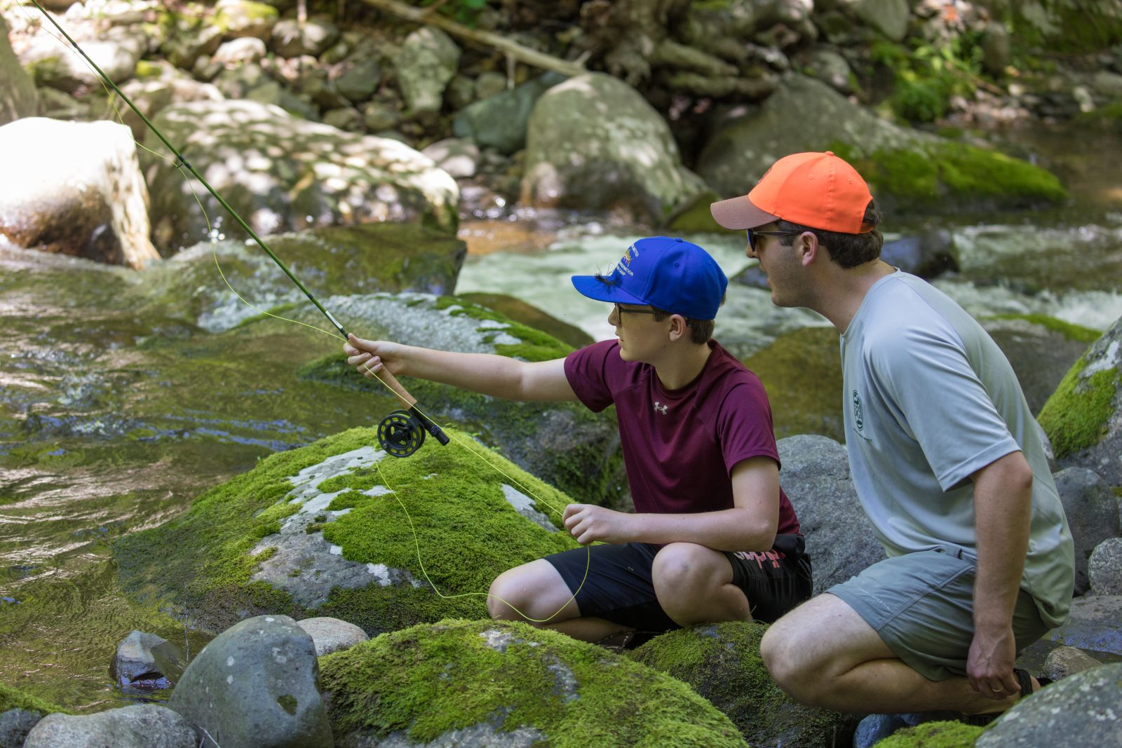 A man and child with a fly rod among moss-covered rocks