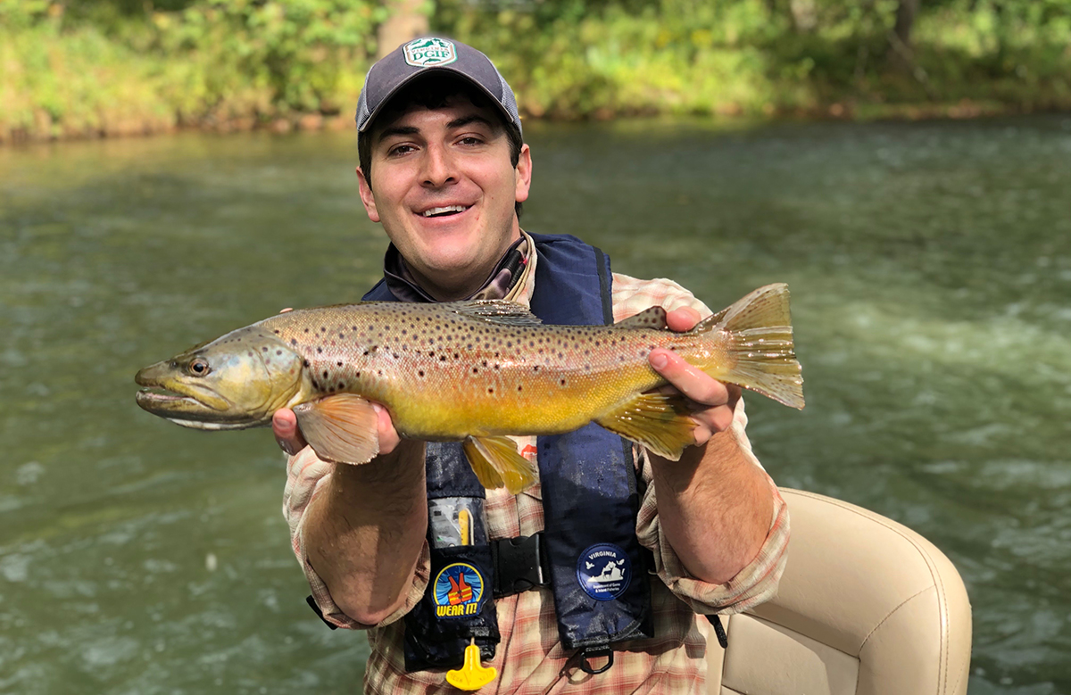 A man smiling at the camera while holding a trout.
