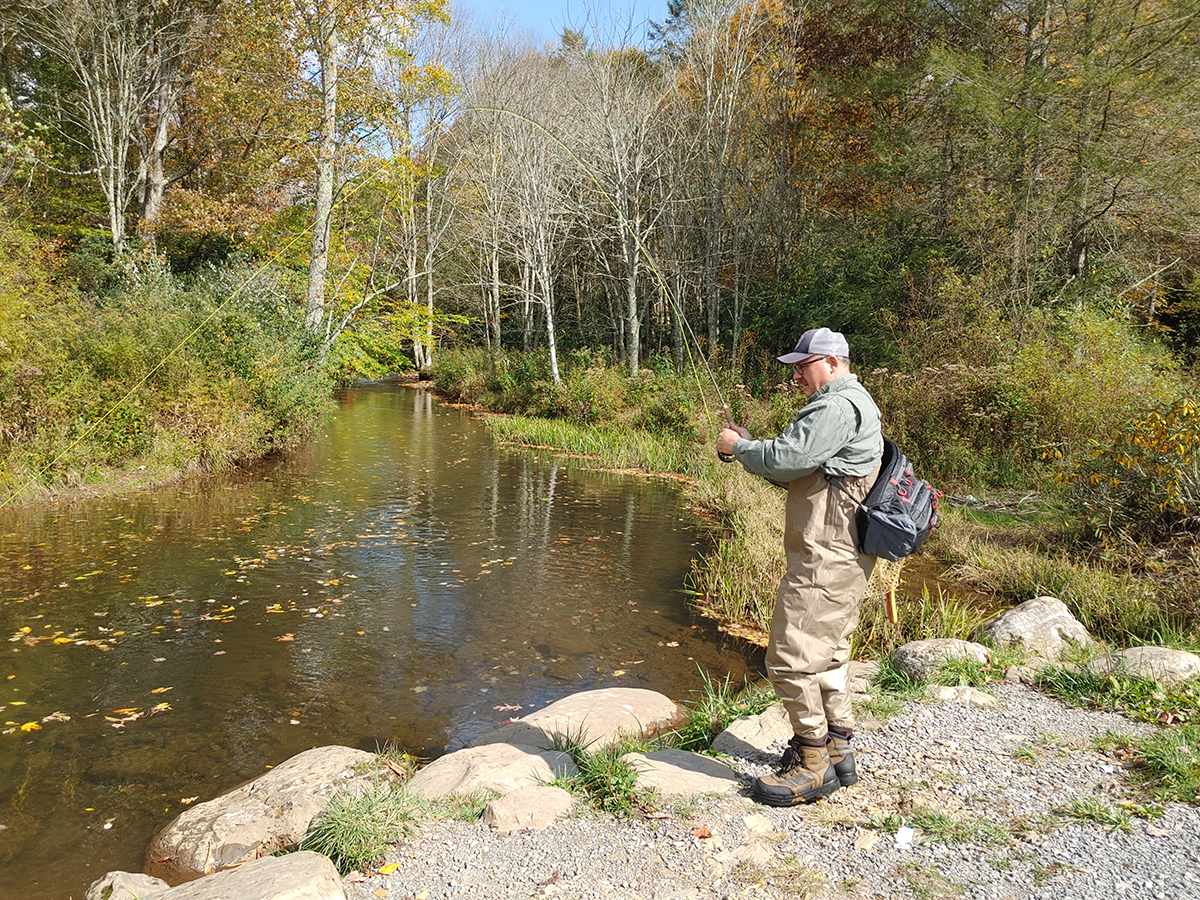 A man fishing a stream from a gravel shoreline.