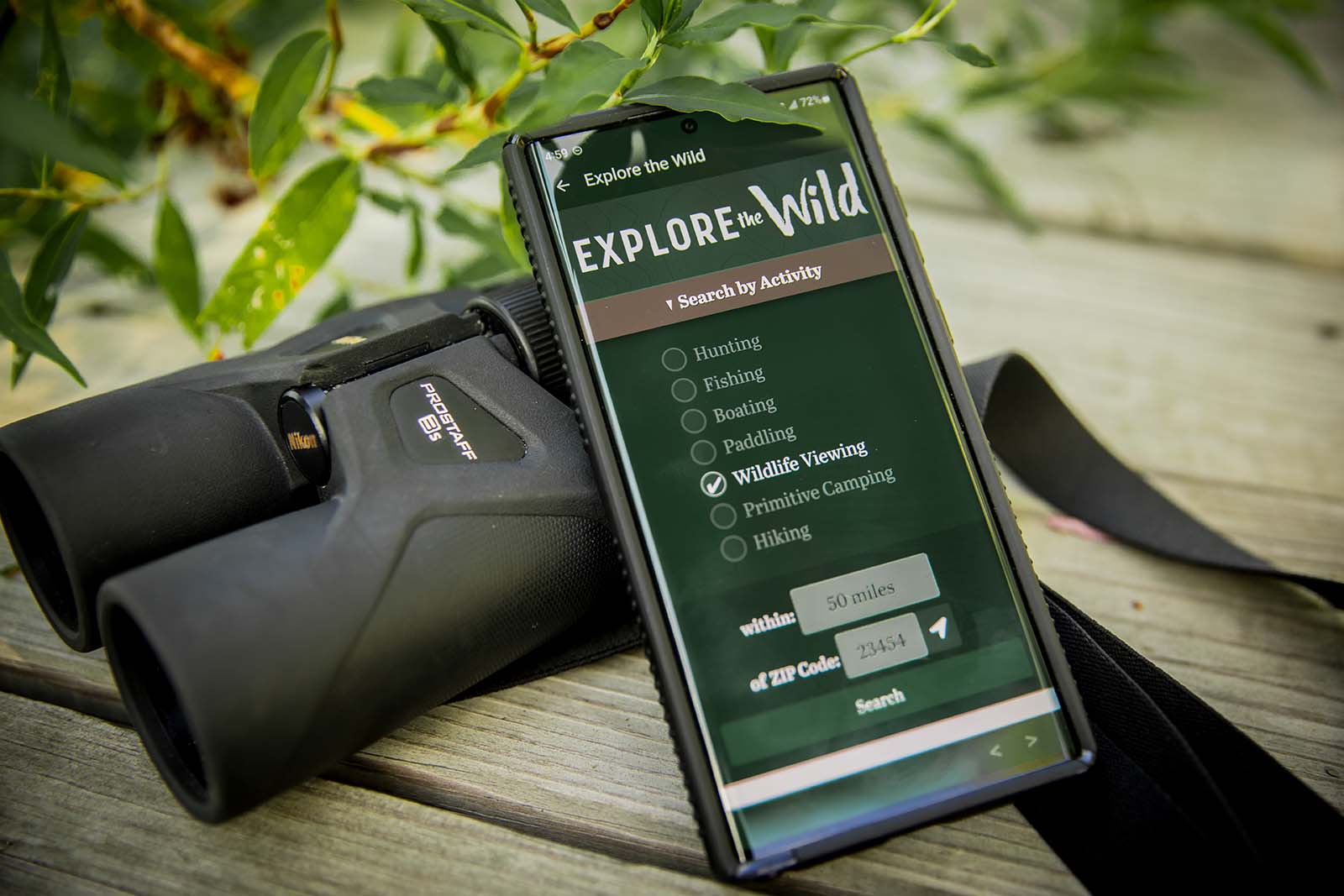 A smartphone showing the Explore the Wild web app, resting against a pair of binoculars