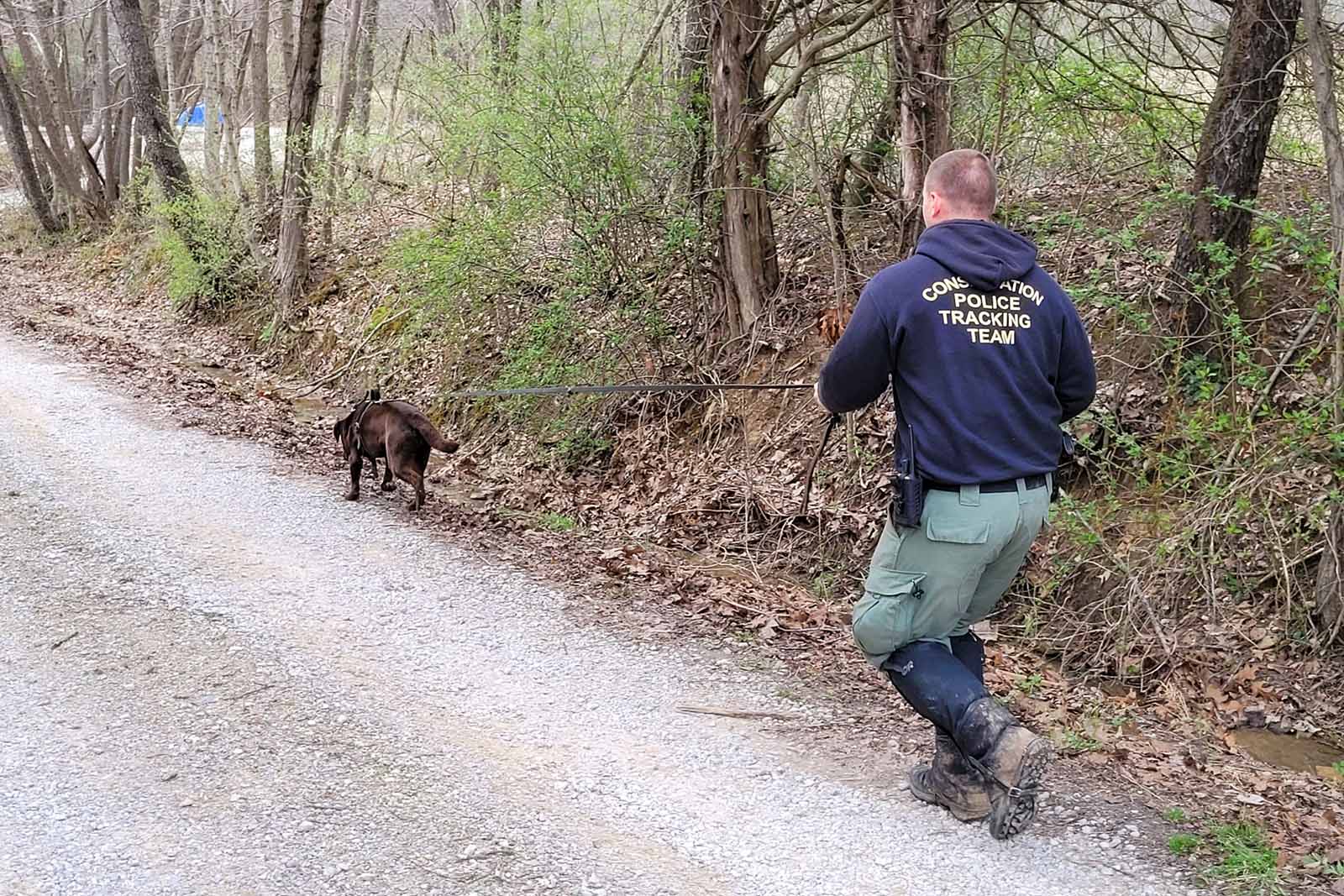 A Conservation Police Officer walking behind a K9 on a leash