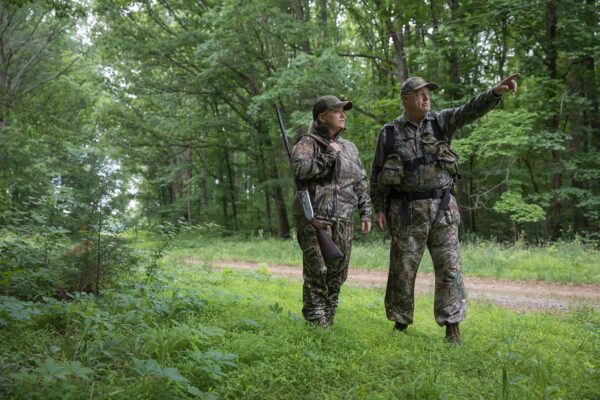 Two hunters in camouflage clothing standing in a clearing pointing into the distance