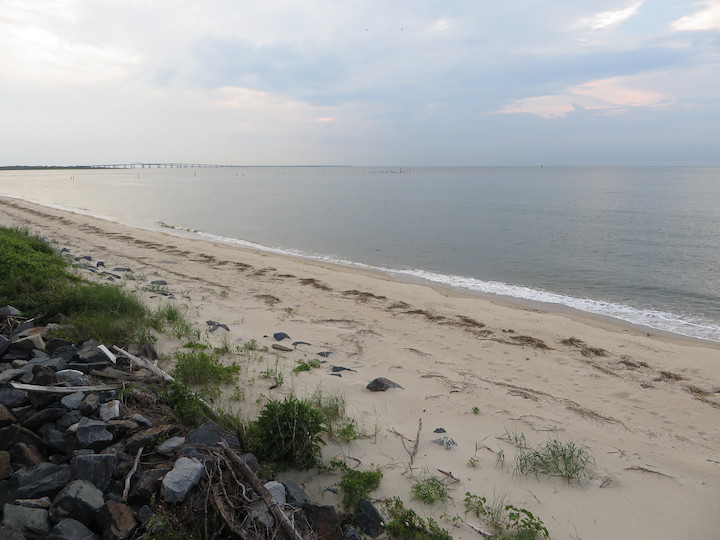 An image of a beach in the Chesapeake bay; it has mild waves and the image was taken atop a stack of rocks overlooking the sandy portion of the shore