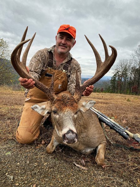 An image of a hunter an an adult buck that he has killed