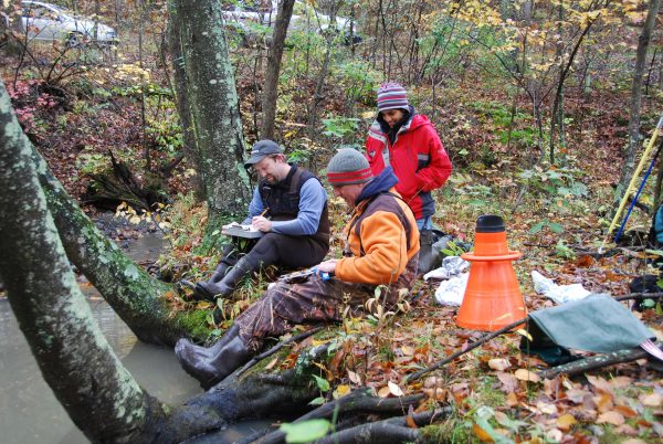 An trio of biologists sitting by a stream recording wood turtle data they gathered during their survey.