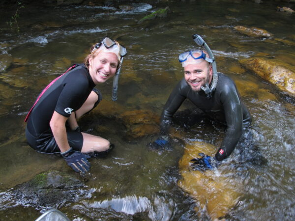 Two people partly submerged in water and wearing wet suits and snorkels.