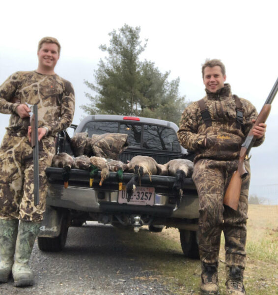 An image of two men posing in front of a truck filled with dead ducks