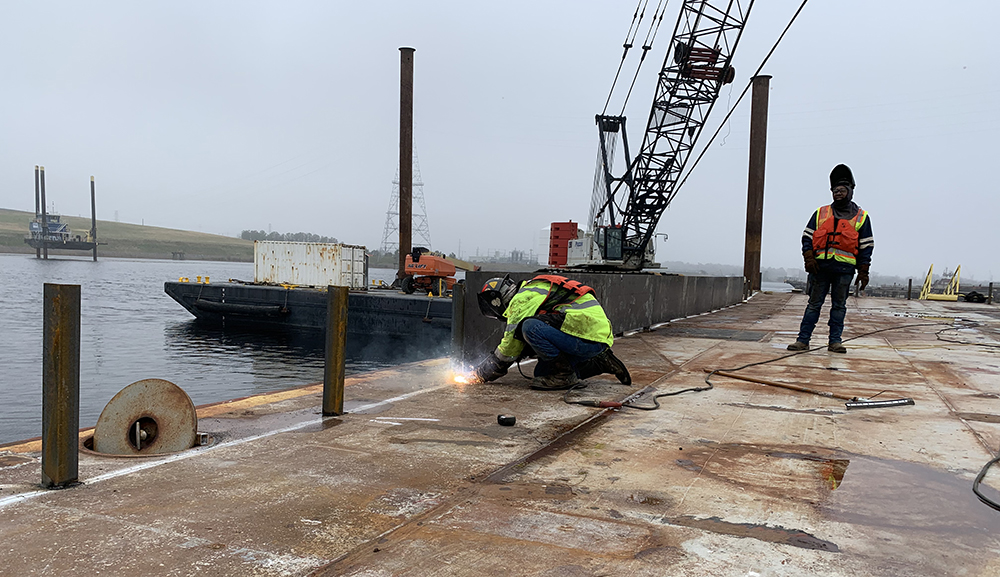 PreCon Marine Construction employees weld a side wall to one of the barges which will be used by the project