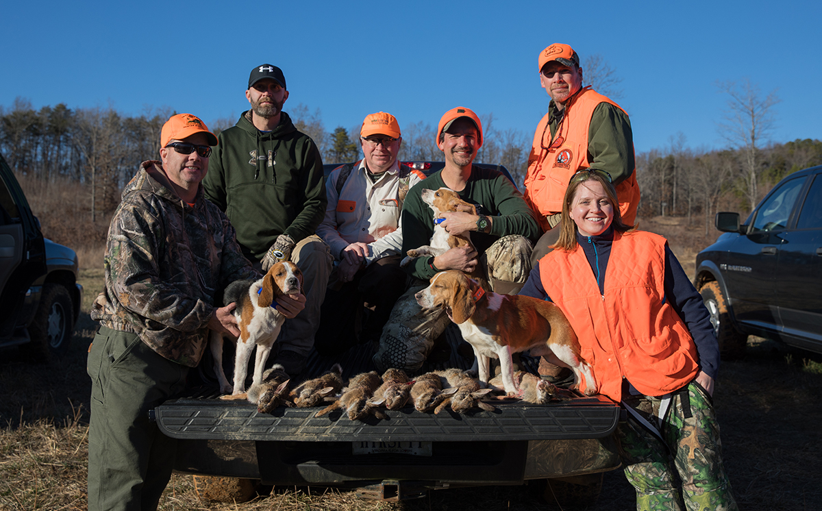 Mindy Tucker and five men and three beagles sitting on a truck containing multiple dead rabbits