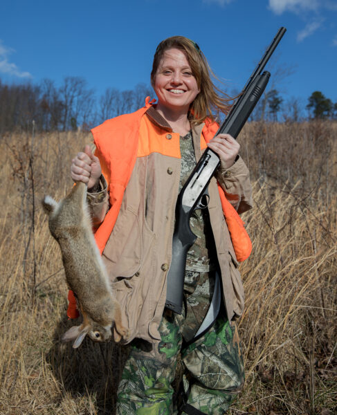 Mindy Tucker in an orange visibility vest with a rifle and a dead rabbit
