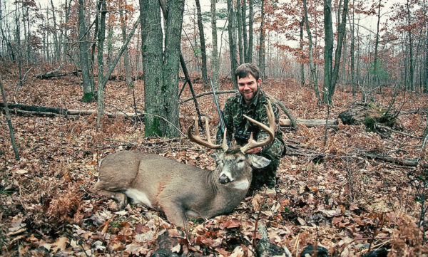 An image of a hunter posing with a dead buck
