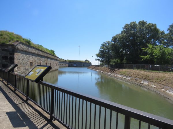 An image of a moat within fort Monroe with a steep windowed cliff on one side and a much smoother grassy field on the other; this image was taken at the visitor center.