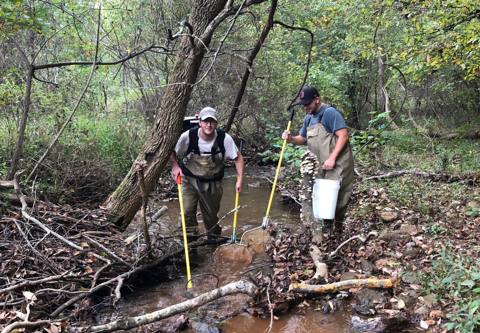 An image of two men electrofishing in a small creek using the backpack equipment which is the same as on the boat but more transportable.