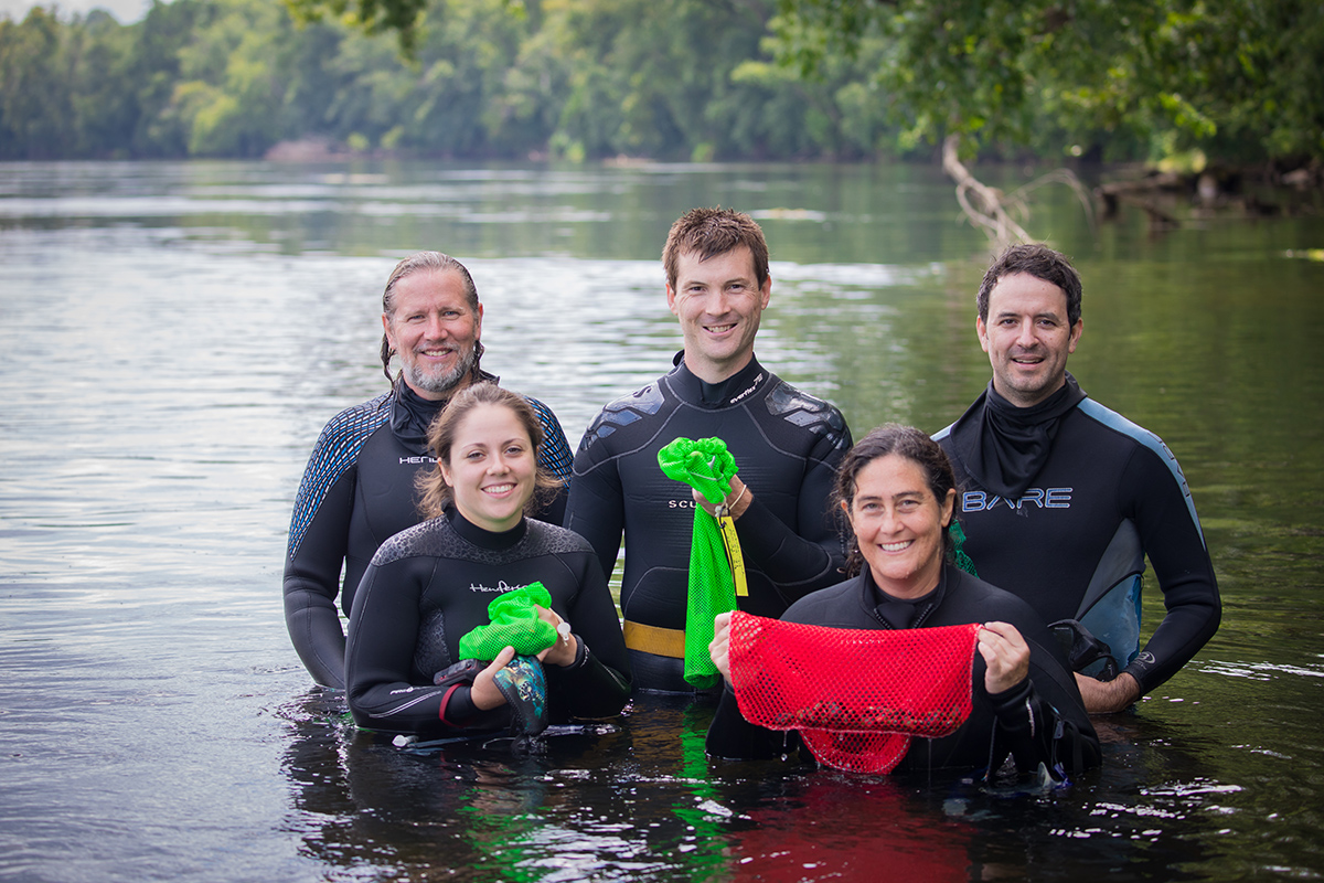 An image of five people posing for a picture in a river; they are holding bags of mussels
