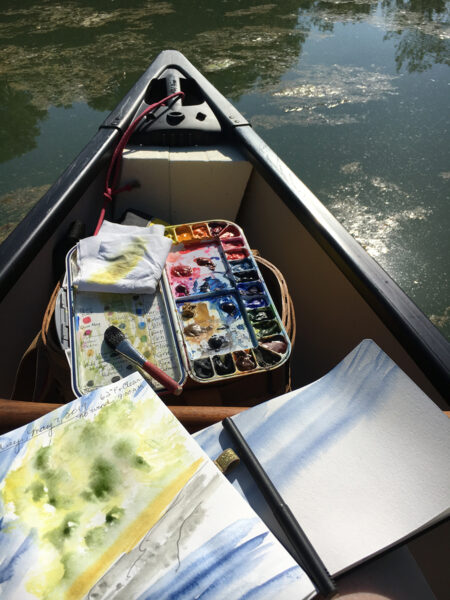 An image of the watercolor journaling supplies on a kayak which is in the water.