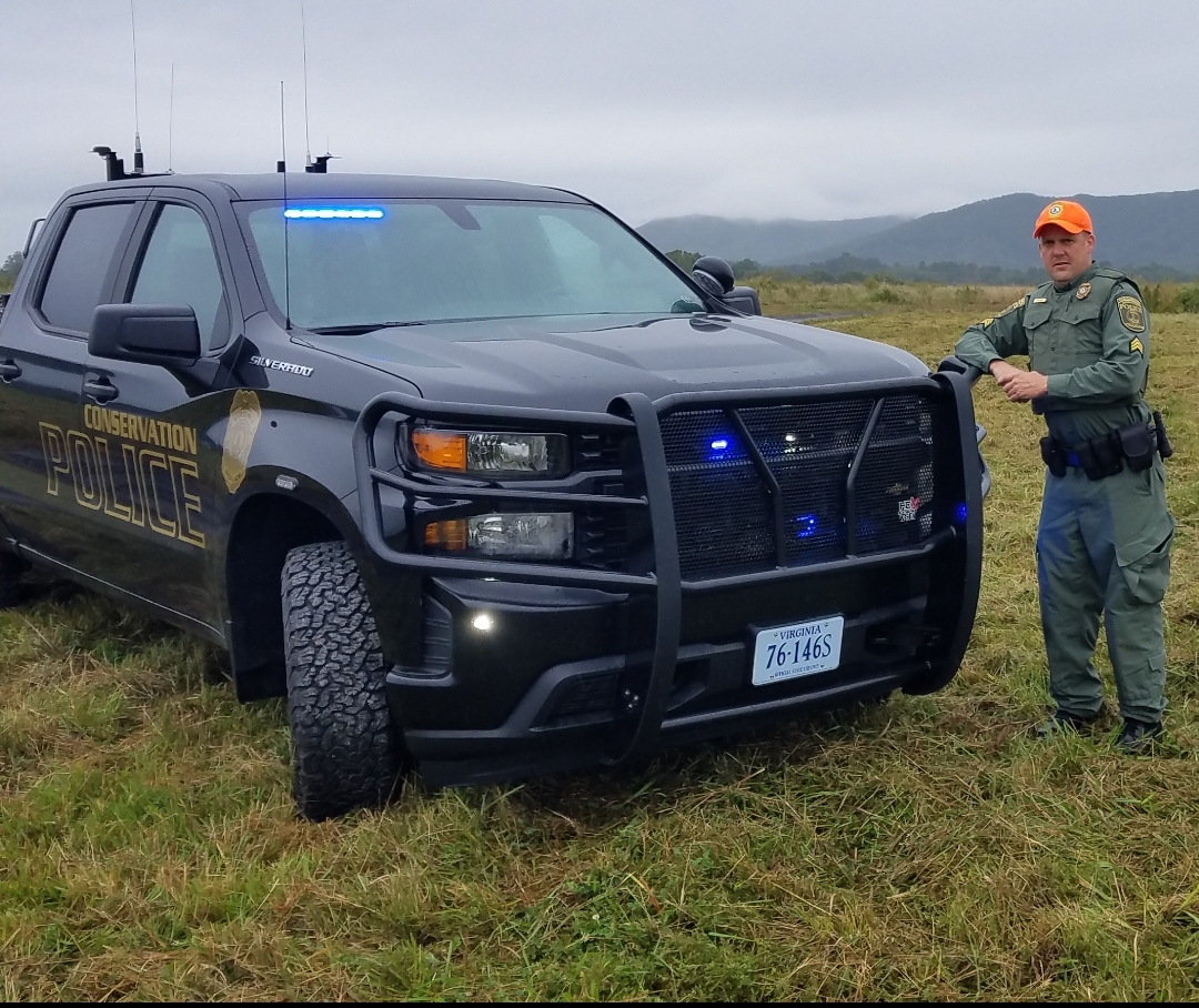 An image of a conservation police officer and vehicle in a meadow