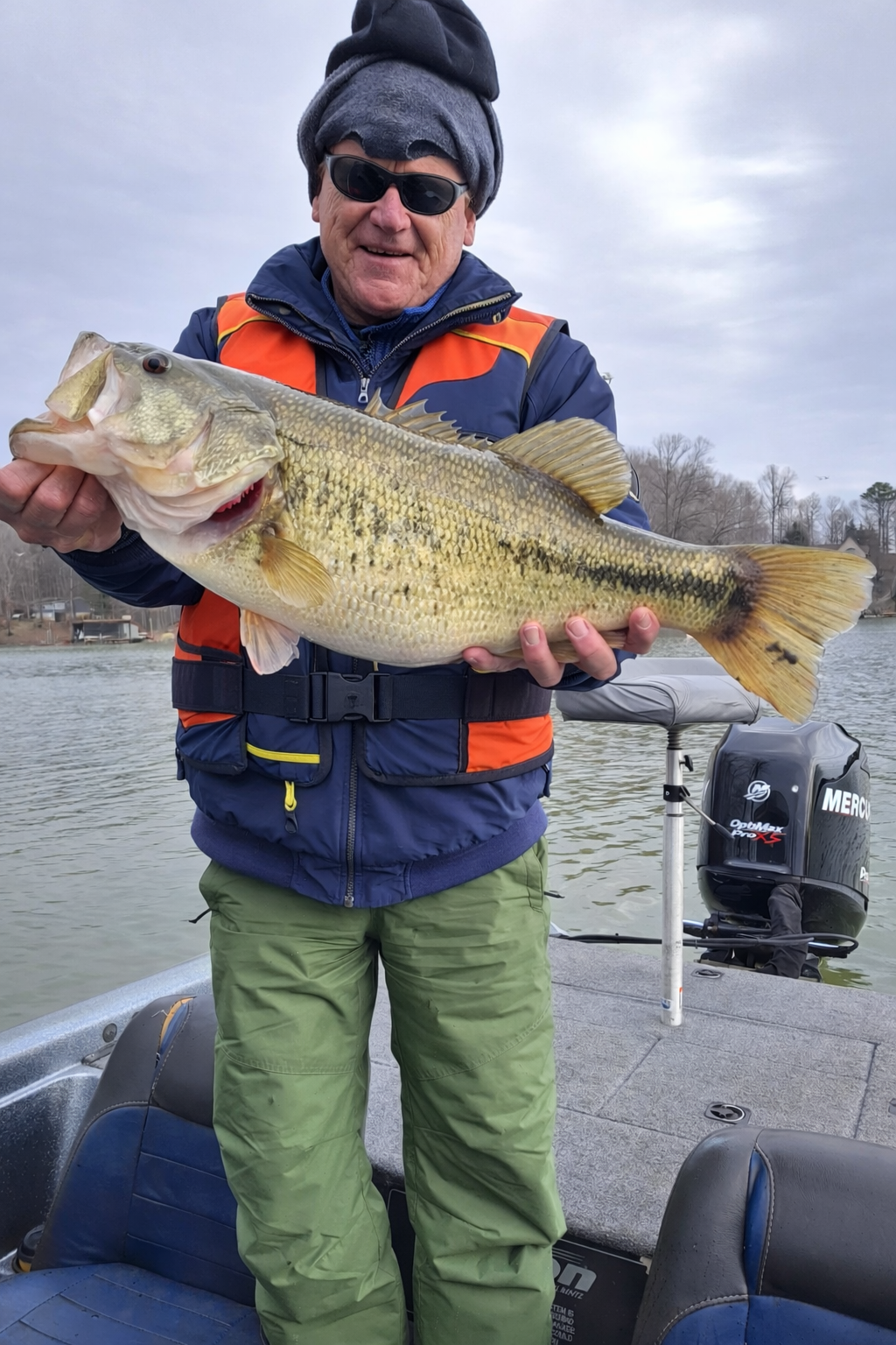 A photo of a man standing in a boat, holding up a large largemouth bass.