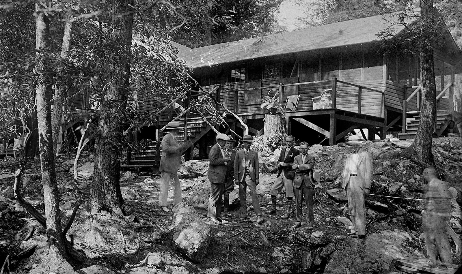 A black-and-white photo of a group of people in 1930s-era clothing standing in front of The Brown House, a wooden residence built on an overlook of the Rapidan River.