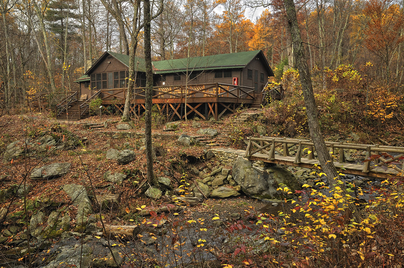 A color photo of The Brown House, as wooden residence built overlooking a rocky slope to a small river. 