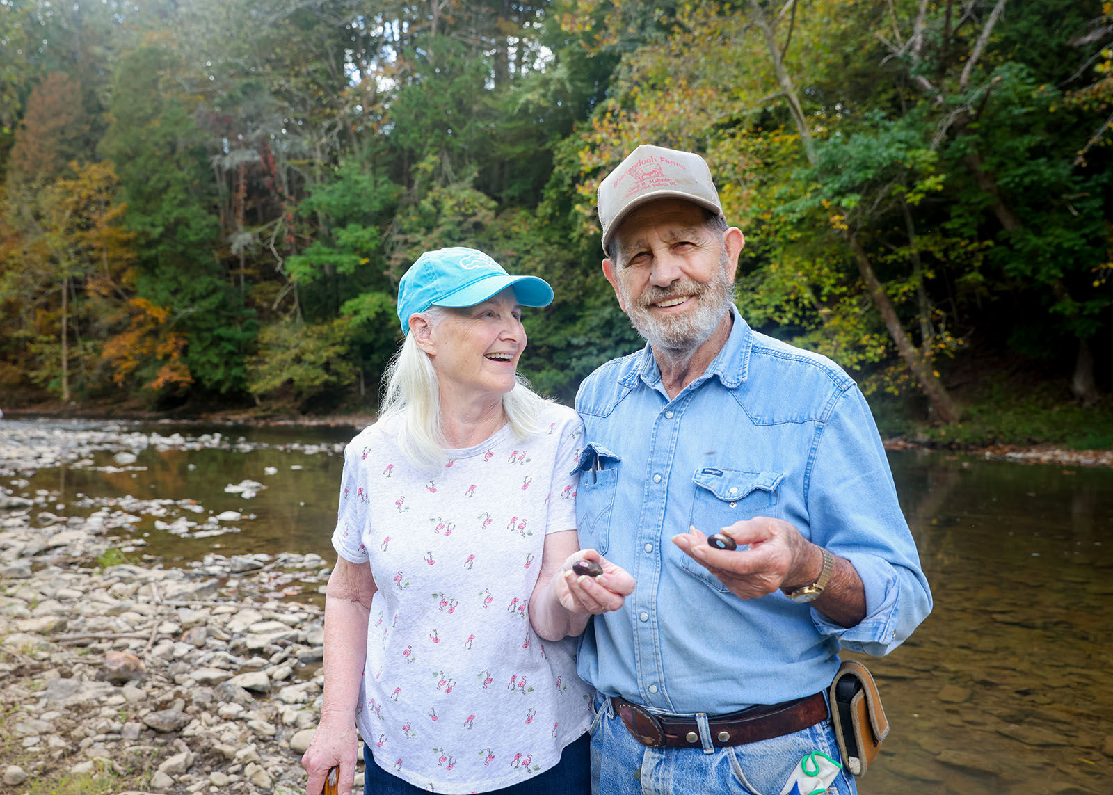 A photo of a man and a woman holding some freshwater mussels and standing in front of a river.