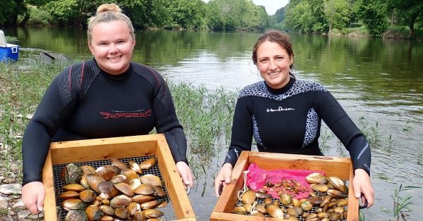 Two women holding trays of mussels during Musselrama in front of a river