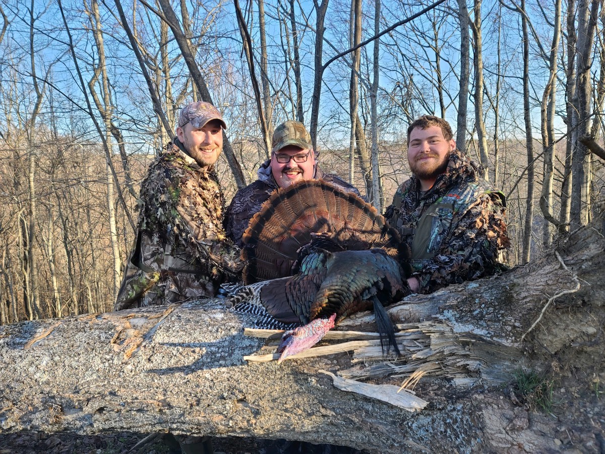 Three men and a dead turkey in a deciduous forest