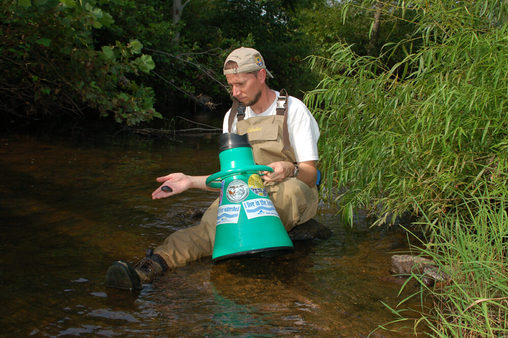 An image of a biologist who used a device to look into the water holding a James Spiny mussel that he had caught