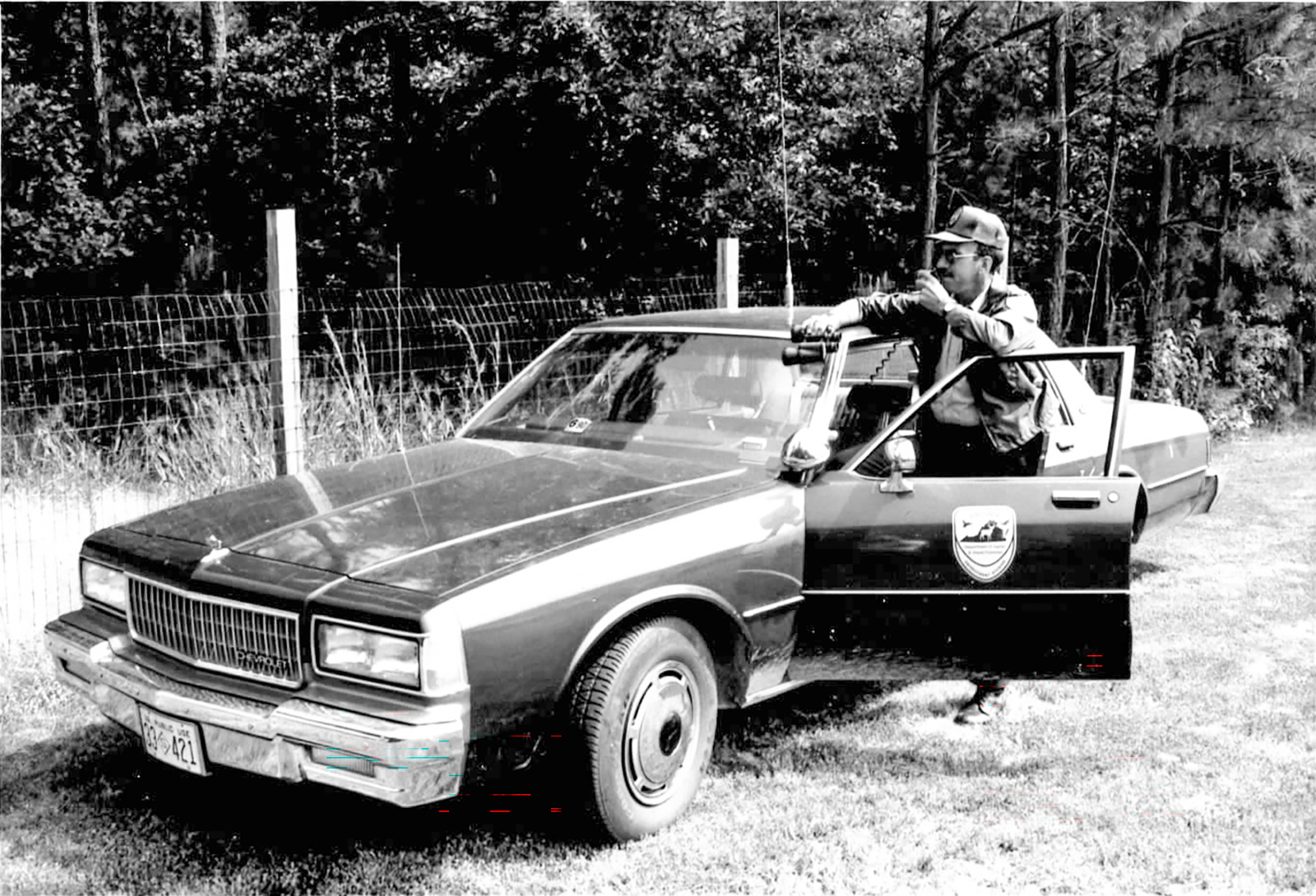 A historic black-and-white photo of a game warden and his vehicle.